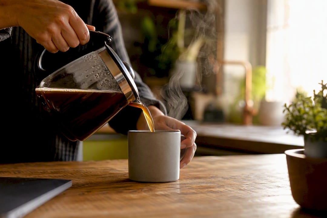 Händer som häller upp kaffe på ett skrivbord på kontoret